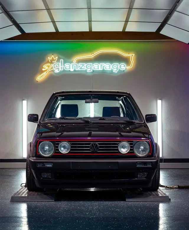 Schwarzer VW Golf 2 unter dem leuchtenden Neon-Schriftzug sj glanzgarage
