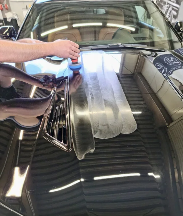 Maschinelle Lackpolitur auf der Motorhaube eines schwarzen Fahrzeugs